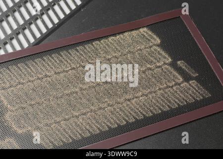 dirty black pc case dust filter mesh on vent grille, heavily coated in thick layer of accumulated dust fibers, top view closeup, computer maintenance Stock Photo