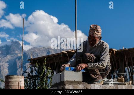A worker in Kalpa using a spirit level, squatting on a wall being built, with the Kinnaur Kailash range in the distance. Stock Photo