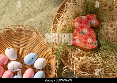 Top view Easter flat lay with floral bunny cookie wicker baskets and pastel speckled eggs on straw background Stock Photo