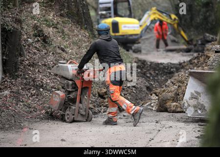 Aufnahme vom 28. Februar 2026 Auf dem Foto ist eine Straßensanierung in Stuttgart zu sehen, auf dem Arbeiter eine beschädigte Fahrbahn aufschneiden und vorbereiten. Im Vordergrund führt ein Bauarbeiter mit Warnkleidung eine motorisierte Fugensäge über den unbefestigten Straßenbelag. Weiter hinten arbeitet ein zweiter Arbeiter neben einem gelben Bagger, der Erdreich aushebt und den Graben erweitert. Die Szene zeigt typische Arbeitsabläufe der Straßensanierung, inklusive schwerem Gerät, offener Baustelle und klar erkennbaren Maßnahmen des Arbeitsschutzes. Feature, Schmuckbild Bauarbeiten, Straße Stock Photo
