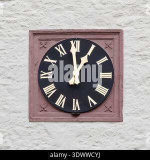 Vintage black wall clock with gold Roman numerals mounted on textured white plaster, evoking timeless elegance and architectural detail; suitable for Stock Photo