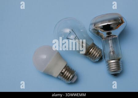 Three light bulbs on a blue background.Two incandescent light bulbs and a third LED lamp on a blue background, flatlay. Stock Photo
