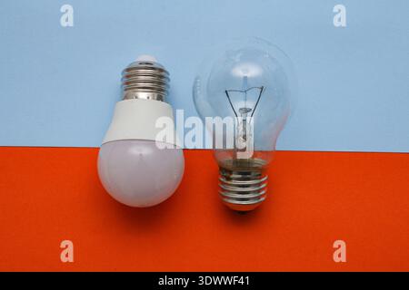 An incandescent light bulb and an LED lamp lie on an abstract blue and red background. Two light bulbs, energy saving concept. Stock Photo