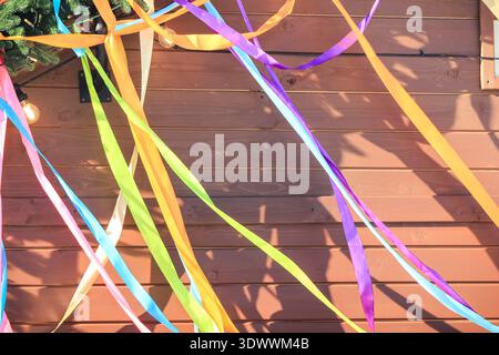 Spring festival bright satin ribbons hanging against a brown wooden wall background with copy space. Stock Photo