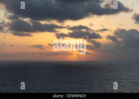 Golden sunrise over open ocean with dramatic clouds and sun rays reflecting on calm sea, Caribbean Sea, February 2026. Stock Photo