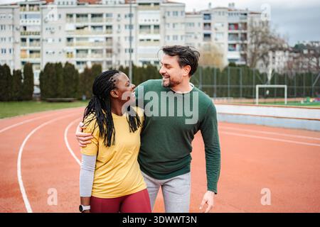 Diverse couple smiling, embracing on running track after workout Stock Photo