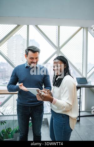 Two people are happily discussing work using a digital tablet Stock Photo