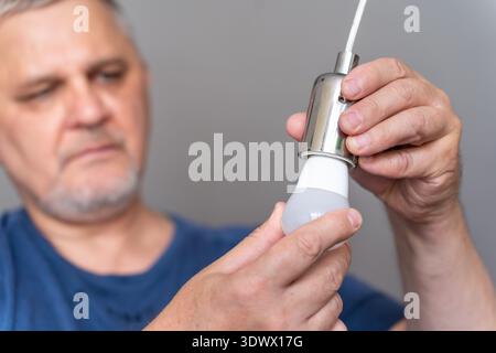 Hands replacing a light bulb in a minimalist room, with focus on the bulb and the clean light fixture Stock Photo