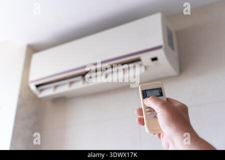 Cropped male hand operating an AC remote in a well-lit room conveys themes of smart living, seasonal regulation, and indoor calm. Scene of remote air Stock Photo