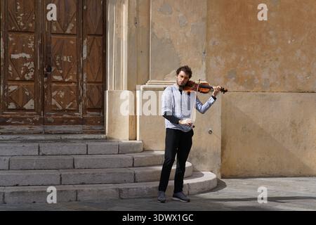 Young violinist busking on historic building steps, passionately playing outdoors in old town.Menton,France Stock Photo