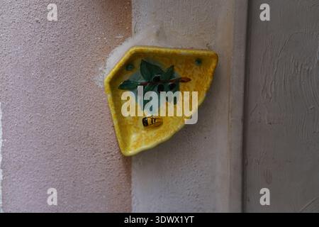 Hand-painted yellow ceramic wall bowl with olive branch motif on rustic Italian house wall.Menton,France Stock Photo