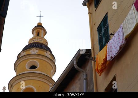 Yellow church tower with onion dome and cross rises beside colorful laundry in Italian village.Menton,France Stock Photo