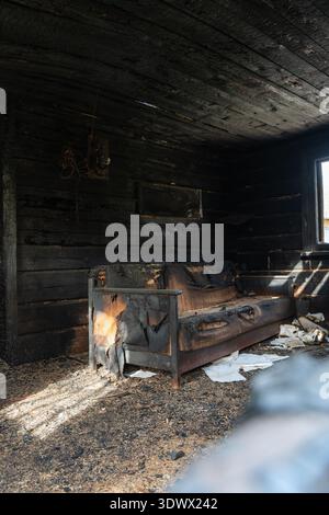 Inside a wooden house ravaged by fire, scorched walls, blackened furniture, and debris litter the floor. Light streams through a cracked window, revea Stock Photo