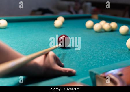 Male Hand Aiming A Cue Stick At The Red Ball On A Green Billiard Table. Stock Photo