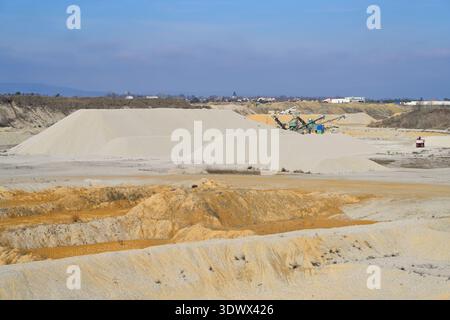 Open pit quarry producing construction material. Industrial site with sand piles, machinery, and truck extracting raw resources. Stock Photo