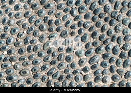 Natural pebble mosaic walkway featuring dark oval stones arranged in irregular pattern, ideal for garden and patio design. Stock Photo