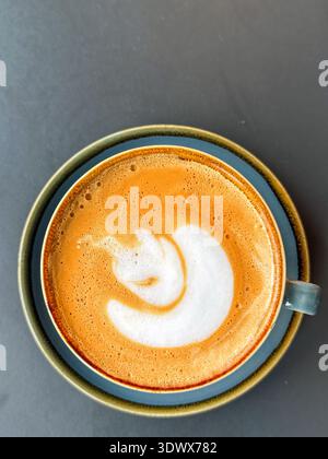 Overhead view of a cup of hot fresh frothy coffee with saucer on a table. No people. Stock Photo