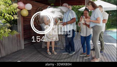 Gathering five adults in summer wear chatting, holding plates on wooden deck with balloons HUD 154 Stock Photo