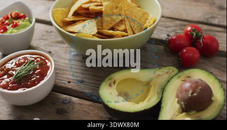 Displaying two halved avocados pit on rustic table pale-green chips-bowl, salsa, guac vine tomatoes Stock Photo