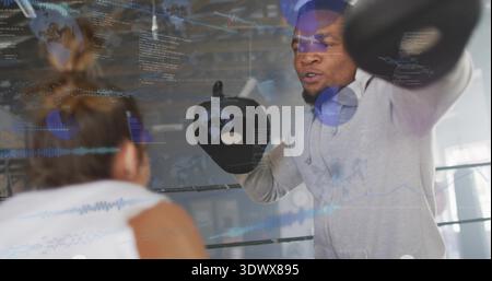 Holding focus mitts gray-hoodie coach bracing trainee in white-top punching gym with data overlay Stock Photo