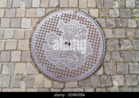A decorative cast iron manhole cover featuring a knight slaying a dragon adorns a cobblestone street in Stein am Rhein, Canton Schaffhausen. A unique Stock Photo