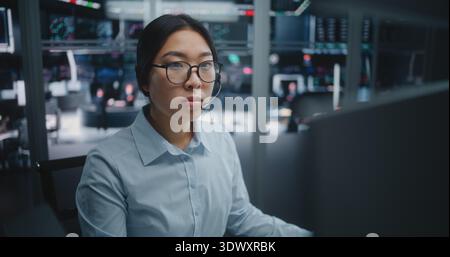 Young Asian Financial Analyst Consulting on Headset in Futuristic Trading Hub. Tech Savvy Female Broker Wearing Headset, Engaged in Deep Data Analysis. Key Decision Maker in Global Financial Market. Stock Photo