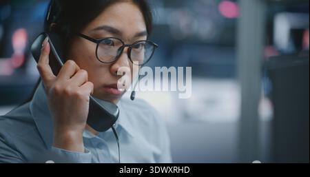 Asian Stock Exchange Trader Manages Live Market Operations While Speaking on Landline Phone and Holding Tablet Displaying Analytical Data. Woman Coordinates Transactions and Reviews Financial Metrics. Stock Photo