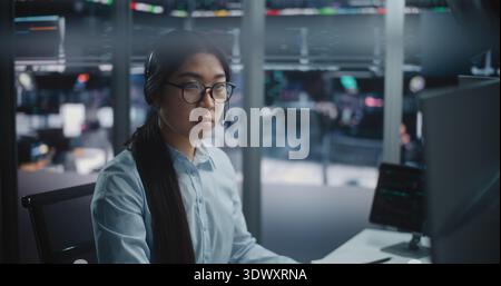 Expert Asian Analyst Scrutinizing Global Economic Trends in Futuristic Digital Office. Stylish Female Professional Completely Absorbed in Work, Navigating Through Vast Amounts of Big Data and Graphs. Stock Photo