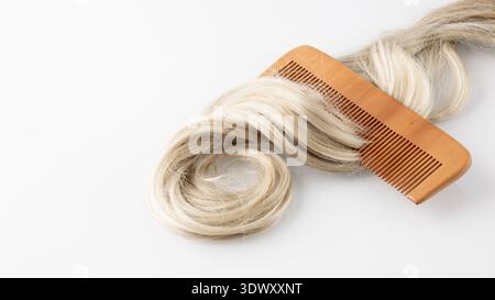 Curled female blonde hair strand with wooden brush on white glass background. Haircare concept. Stock Photo