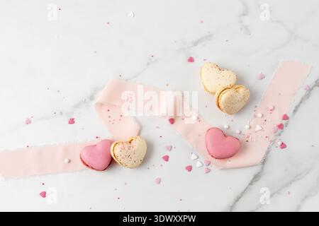 French sweet cookies macarons macaroon with color sprinkles with silk ribbon on marble table background. Heart shape macarons, cupcake and decor. Mock Stock Photo