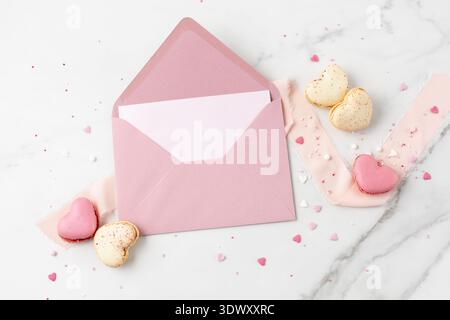 Blank paper card and open retro pink envelope with macarons macaroons in heart shape and sprinkles on white marble background. Mockup birthday or vale Stock Photo