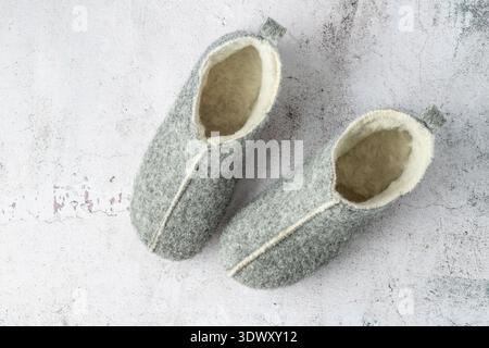 Grey felt wool home winter pair slippers on stone floor background. Warm soft cozy footwear for house. Stock Photo