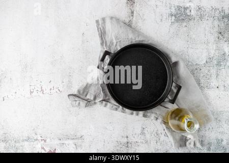 Empty black cast iron pan or serving plate and olive oil bottle over grey linen towel. Mockup with space for your tasty dinner dish on retro stone tab Stock Photo