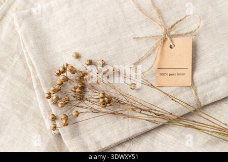 Dried flax plant bunch on folded natural beige linen fabric with rope and text 100% Pure Linen. Floral background in vintage style with copy space Stock Photo