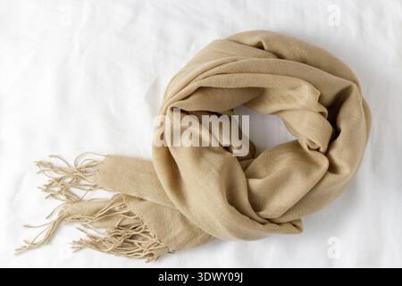 Beige classic soft scarf made of fine pure cashmere with tassels on white linen background Stock Photo