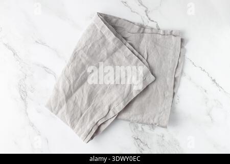 Wrinkled light grey soft pure linen serviette or napkin on white marble board. Folded natural linen napkin on light marble background with copy space. Stock Photo