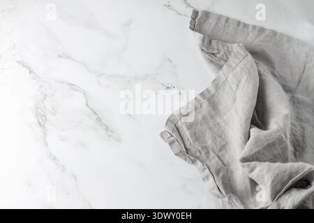 Wrinkled light grey pure linen towel on empty white marble board. Light marble background with copy space. Stock Photo