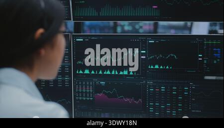 Woman Engages With Real Time Stock Data on Multiple Analytical Displays in Vast, Innovative Digital Hub. Concept of Seamless Global Communication and Professional Expertise in Futuristic Workspace. Stock Photo