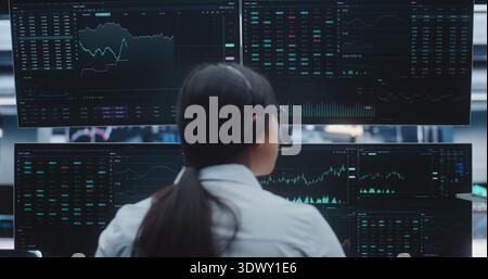 Asian Female Broker Monitors Real Time Indices in Massive Digital Trading Room. Concept of Corporate Strategy, Institutional Investing and Innovative Corporate Infrastructure in Heart of City. Stock Photo
