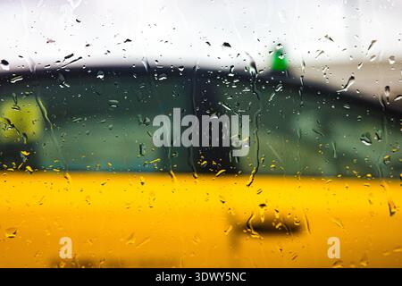 Rain drops on window glass with blurred urban background during rainy day Stock Photo