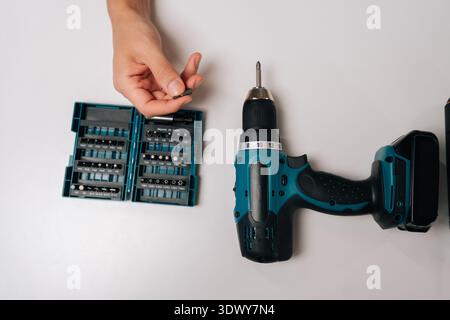 Close-up of male hand choosing precision bit from organized set, readying powerful teal and black cordless impact driver for assembly or repair work Stock Photo