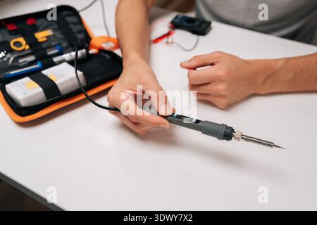 Hands holding soldering iron, adjusting temperature settings with buttons, focusing on electronics repair, creating and prototyping in a workshop Stock Photo