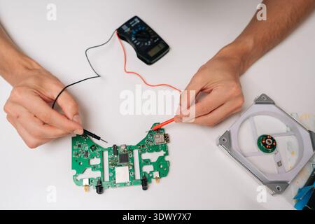Top view of repairman hands troubleshooting game controller circuit board with multimeter, checking electronic components and diagnosing potential Stock Photo