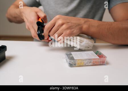 Cropped shot of technician hands holding cable crimping tool, preparing white electrical wire for secure connection, performing precise task of Stock Photo
