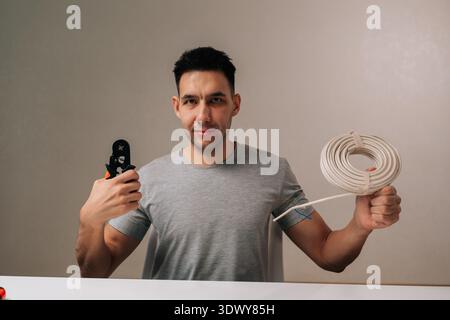 Portrait of young man smiling looking at camera, holding cable crimping tool in one hand and coiled wire in other, symbolizing expertise in electrical Stock Photo