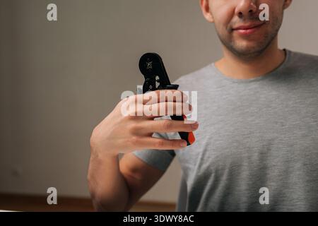 Cropped shot of electrician male holding network cable crimping tool, demonstrating professional skill and precision in electronic repair Stock Photo