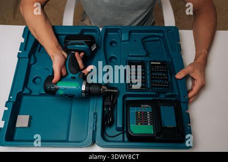 Top view of handyman showing cordless power drill, battery charger and many assorted screwdriver bits inside sturdy turquoise tool case, ready for Stock Photo