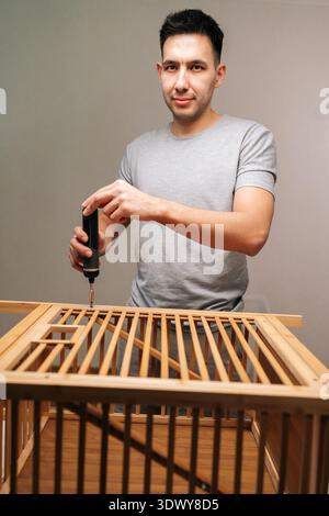 Vertical portrait of handyman using precision electric cordless screwdriver to assemble flat-pack furniture, focusing on diy home improvement and Stock Photo