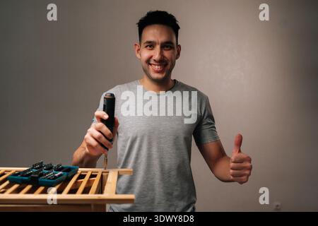 Portrait of happy man installing and building wooden furniture components with electric screwdriver, showcasing successful home assembly and Stock Photo