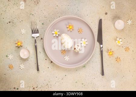 Elegant easter table setting featuring a plate with speckled chicken and quail eggs, surrounded by decorative white and yellow spring flowers, cutlery Stock Photo